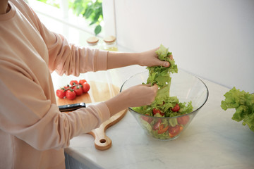 Young woman cooking salad at table in kitchen, closeup