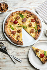 Delicious cheese pizza with walnuts and grapes served on white wooden table, flat lay
