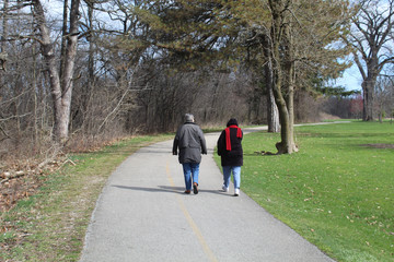 Two older women, one with a bright red scarf, walking on the North Branch Trail in early spring at Linne Woods in Morton Grove, Illinois