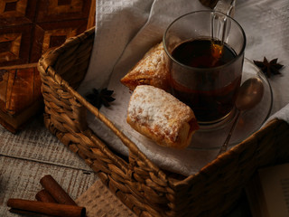 Tea with sweet cookies in a wicker tray on white wooden background. Cinnamon stiks lay near the afteroon tea