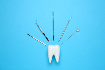 Ceramic model of tooth and dentist tools on light blue background, flat lay