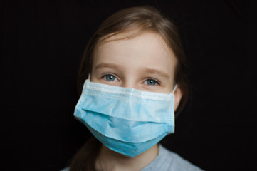 Coronavirus Covid-19 outbreak. Little blonde girl with blue eyes wearing disposable mask for protection of virus on black background in studio. Personal protective equipment concept