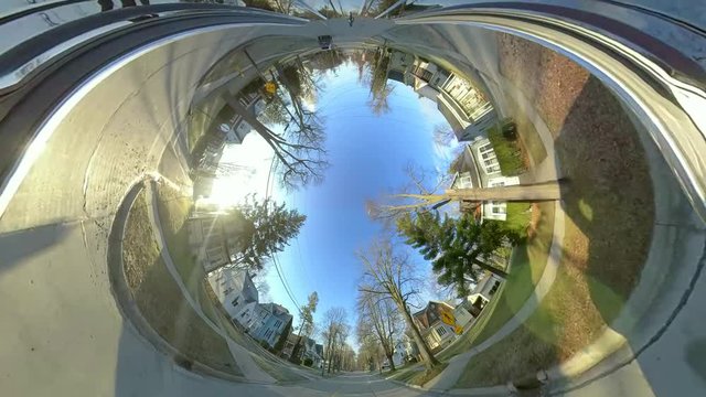 Driving through neighborhood houses in springtime, strange tunnel perspective, morphing into tiny planet perspective.