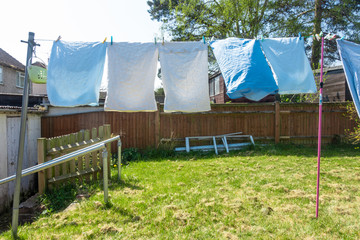 Bedding and sheets are freshly laundered and are hanging out to dry on a washing line in residential back garden.