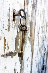 Key in the lock of an old weather shed door with flaky white paint.