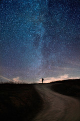 Achteraanzicht van een man die op een onverharde weg staat onder de sterrenhemel