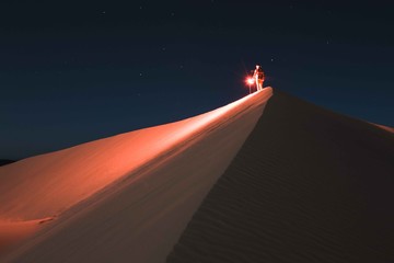 Man with red light standing on sand dune at night