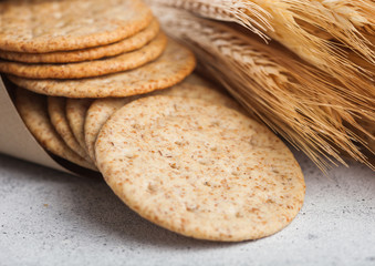 Round organic crispy wheat and corn flatbread crackers with raw wheat on light background.