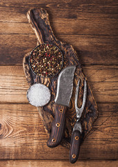 Vintage fork and knife for meat on wooden chopping board with salt and pepper on wooden table background.