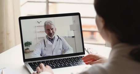 Senior male doctor videoconferencing woman remote patient consulting about corona virus pandemic during telemedicine video call in conference virtual webcam chat app. Over shoulder laptop screen view. - Powered by Adobe