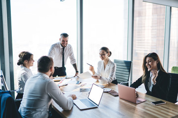 Manager laughing while standing and speaking to colleagues on meeting