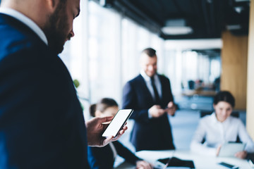 Bearded businessman browsing smartphone during conference with colleagues