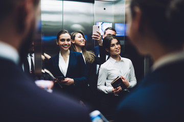 Joyful coworkers posing and taking selfie while standing in elevator together