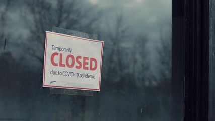 FIXED view of a Temporary closed due COVID-19 pandemic sign hanging on a window. Coronavirus pandemic, small business shutdown - Powered by Adobe