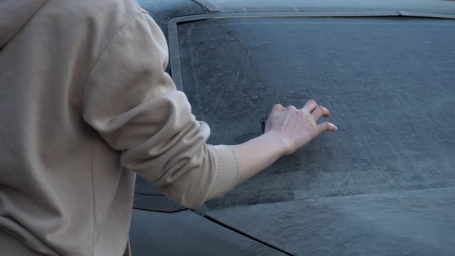 A young woman writes with a finger on a dirty car "please wash me." Prank girl over the car owner. The car is covered in mud.