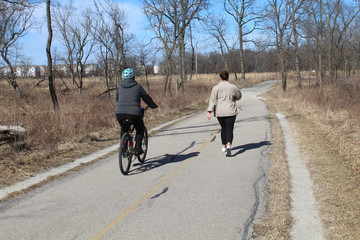 Woman on a bicycle passing up another woman on the North Branch Trail at Miami Woods in Morton Grove, Illinois