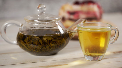 Close up of green tea in teapot and cup on white wooden table.