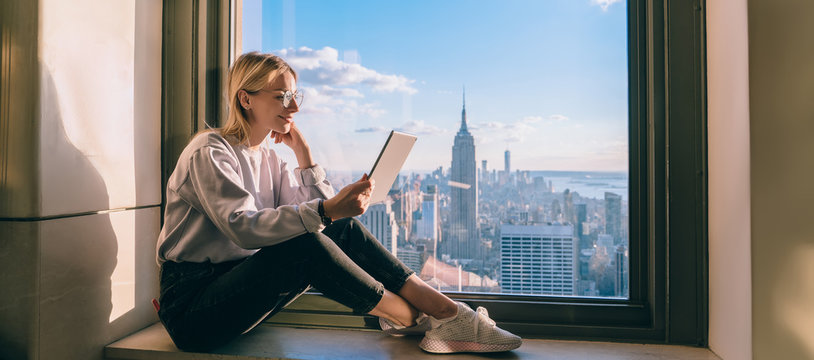 Carefree digital nomad reading social publication with positive content text connecting to 4g wireless on modern touch pad, Caucasian blogger working remotely in highrise with lookout on Manhattan - Powered by Adobe