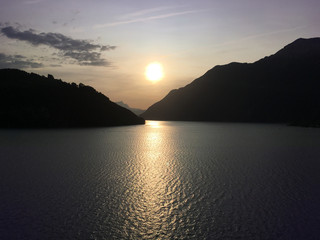 The sun sets over Lake Como sheltered by the Swiss and Italian Alps casting long shadows over the golden lake with a purple sky.