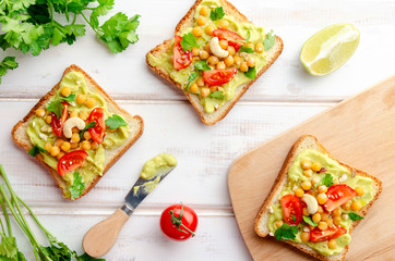 Vegan sandwich with avocado, nuts, vegetables and olive oil on white wooden table