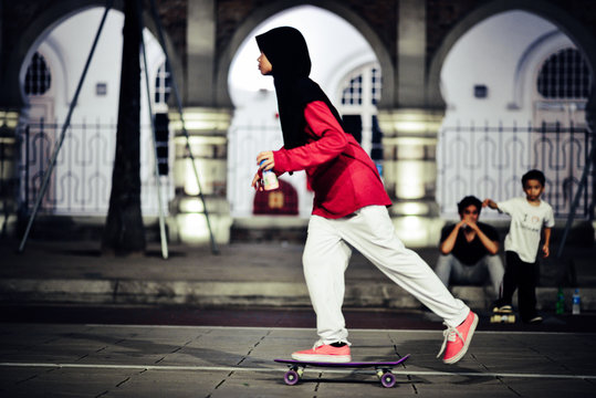 Side View Of Teenage Girl Skateboarding On Footpath At Night