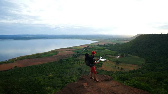 man traveler with backpack looking at the map on the edge of cliff