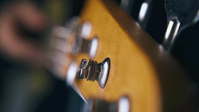 CU: professional guitarist tunes bass guitar stainless steel strings with silver tuning keys on foreground extreme closeup