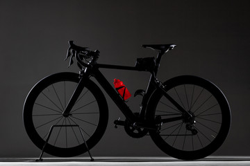 Fototapeta na wymiar Black carbon roadbike with red water bottle on dark studio background
