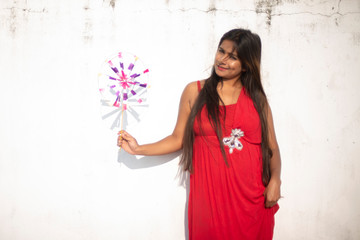 An young and attractive Indian brunette woman in red western dress enjoying with a pinwheel on the rooftop in a morning. Indian lifestyle and quarantine.