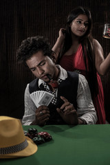 A brunette and young couple in vintage suit and gown playing poker on a green casino table in front of a textured background. Gambling and addictive lifestyle