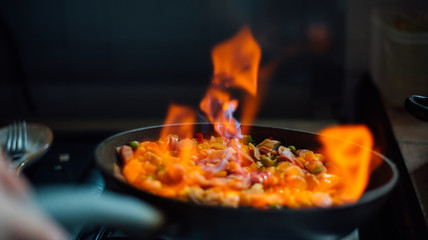 vegetables, onion, pea, carrot, peppers, sausage, ham in a pan flamed with fire