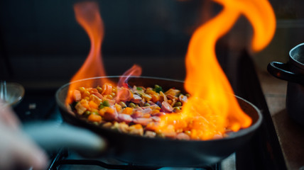 vegetables, onion, pea, carrot, peppers, sausage, ham in a pan flamed with fire