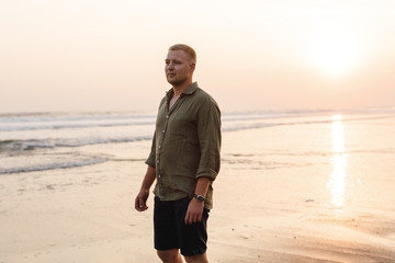 Handsome happy man wearing at the sea or the ocean background. Travel vacation holiday. Man walking at the sea, enjoy tropical season. Relax caucasian adult man looking away at sunset