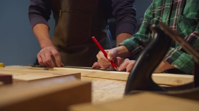 Boy with pencil makes serifs on a wooden board. Garage workshop