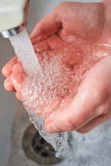 Fototapeta premium Hands holding water with big bubbles and dropping under the faucet while washing with light reflections on the palms for coronavirus prevention