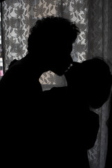 Silhouette of an Indian romantic couple kissing in front of a window. Intimate couple lifestyle 