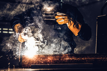 Metal welder working with arc welding machine to weld steel at factory while wearing safety...