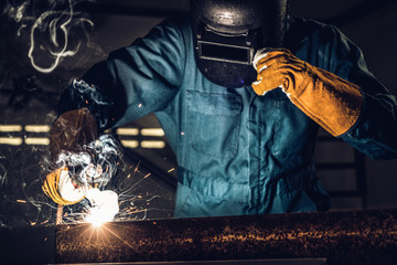 Metal welder working with arc welding machine to weld steel at factory while wearing safety...