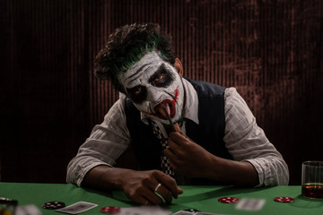 Portrait of an Indian man in Halloween costume showing scary facial expression in front of a casino poker table. Cosplay photography.