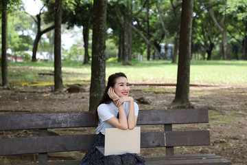 Obraz premium Young asian chinese woman outdoor on park bench use laptop computer think read look happy wonder smile look front retro hand on cheek