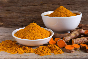Turmeric powder in a white bowl and fresh turmeric  (curcumin) on a wooden table,Used for cooking and as herbal medicine,copy space.