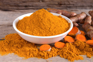 Turmeric powder in a white bowl and fresh turmeric  (curcumin) on a wooden table,Used for cooking and as herbal medicine.