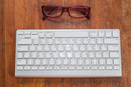 Directly Above Shot Of Computer Keyboard And Eyeglasses On Wooden Table