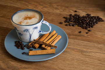 Coffee, cinnamon sticks and roast coffee beans in a blue plate on a wooden table.