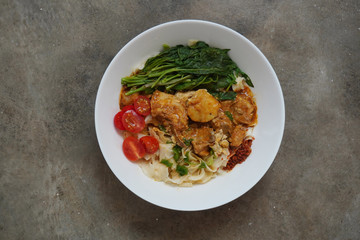 Homemade Dried curry chicken noodles with fresh vegetables at Malaysia. Authentic Malaysian style curry noodles. Flavorful curry soup eaten together with noodles and all it's trimmings.