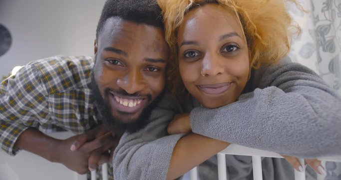 Smiling happy african couple watching infant baby in crib