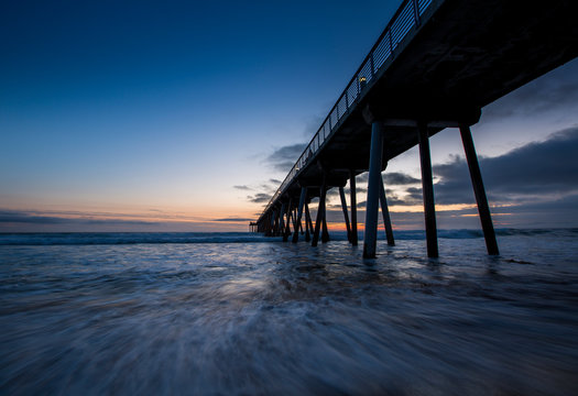 Long exposure of waves rushing in underneath the Hermosa Beach Pier just after sunset in Hermosa Beach, California.