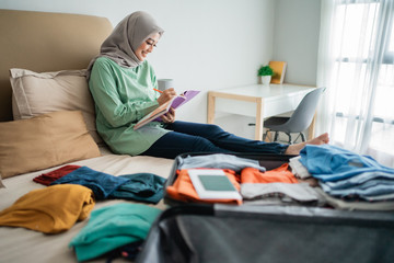 Obraz premium veiled woman sitting on the bed while looking at the list of items to be taken away on vacation