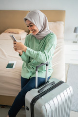 veiled woman sat on the bed holding her smartphone and suitcase before going on vacation