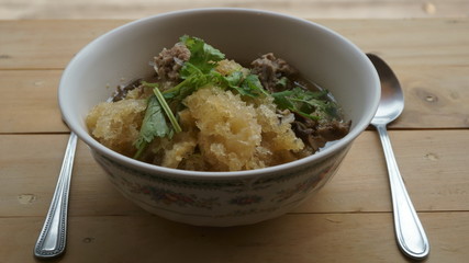 Boiled glass noodles with minced pork on a wooden table